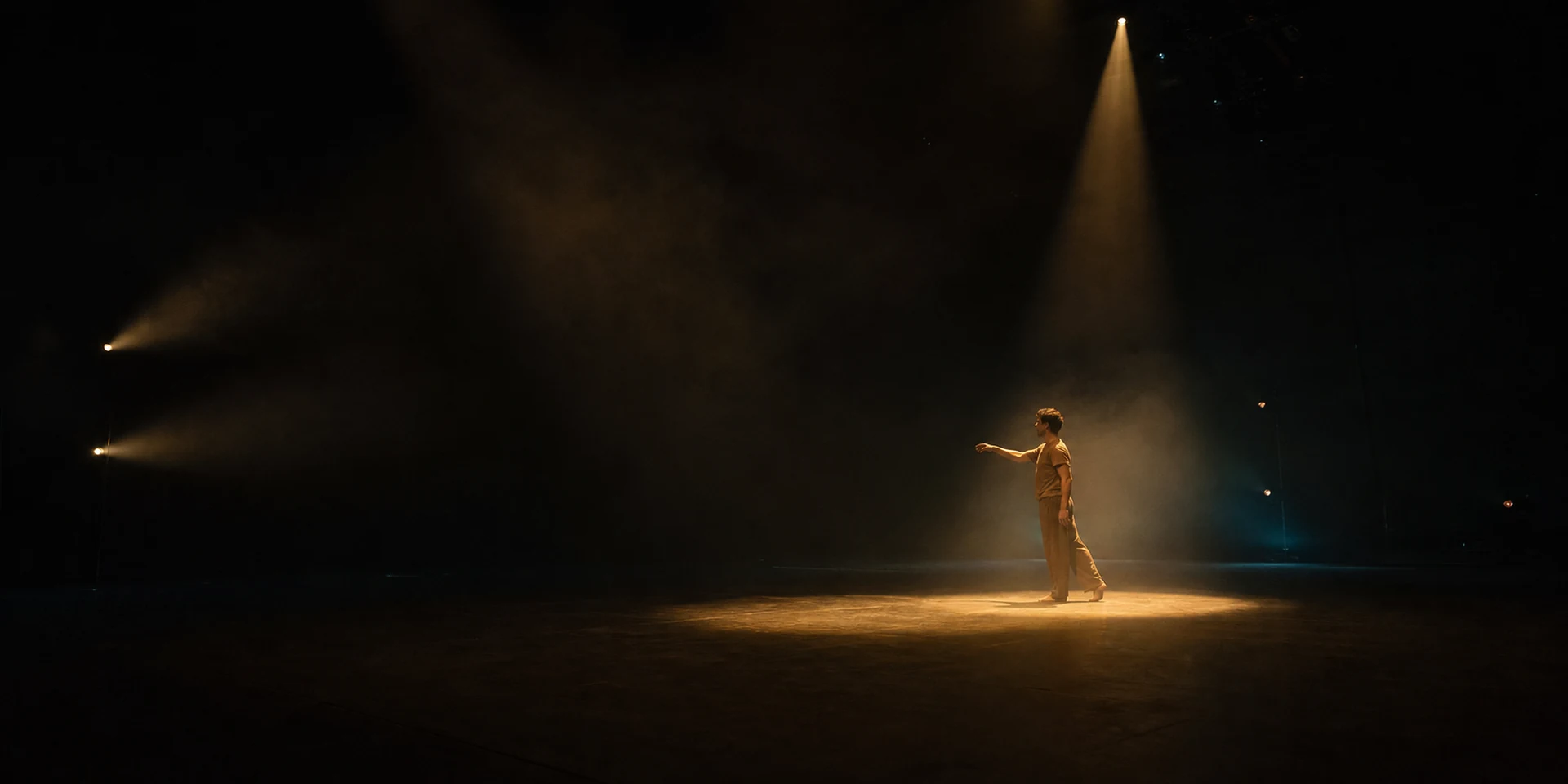 Een performer beweegt door een precies gestuurde poel warm toneellicht